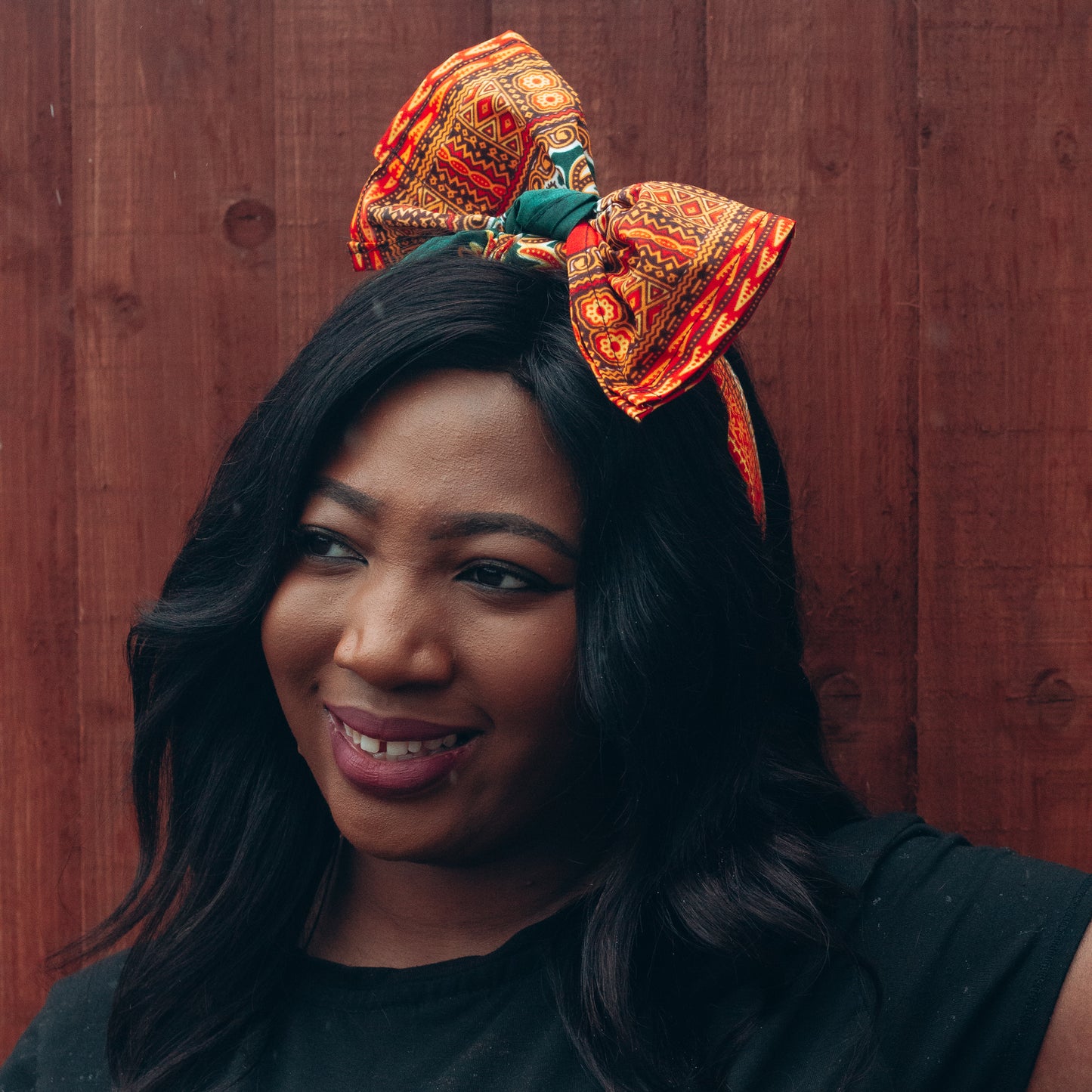 Orange, yellow, red and green African print head wrap tied as headband in a medallion panel pattern, made from sustainably sourced Ankara wax print. 