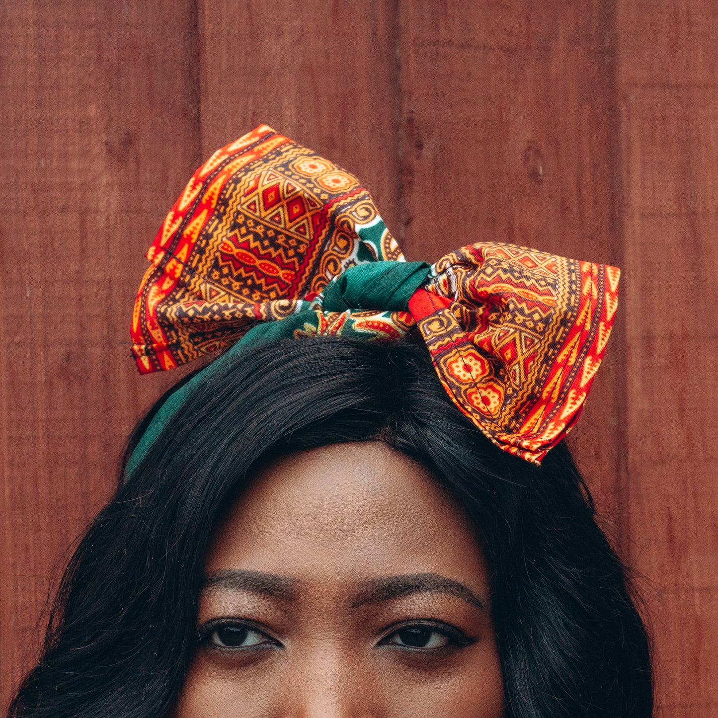 Orange, yellow, red and green African print head wrap tied as headband in a medallion panel pattern, made from sustainably sourced Ankara wax print. 