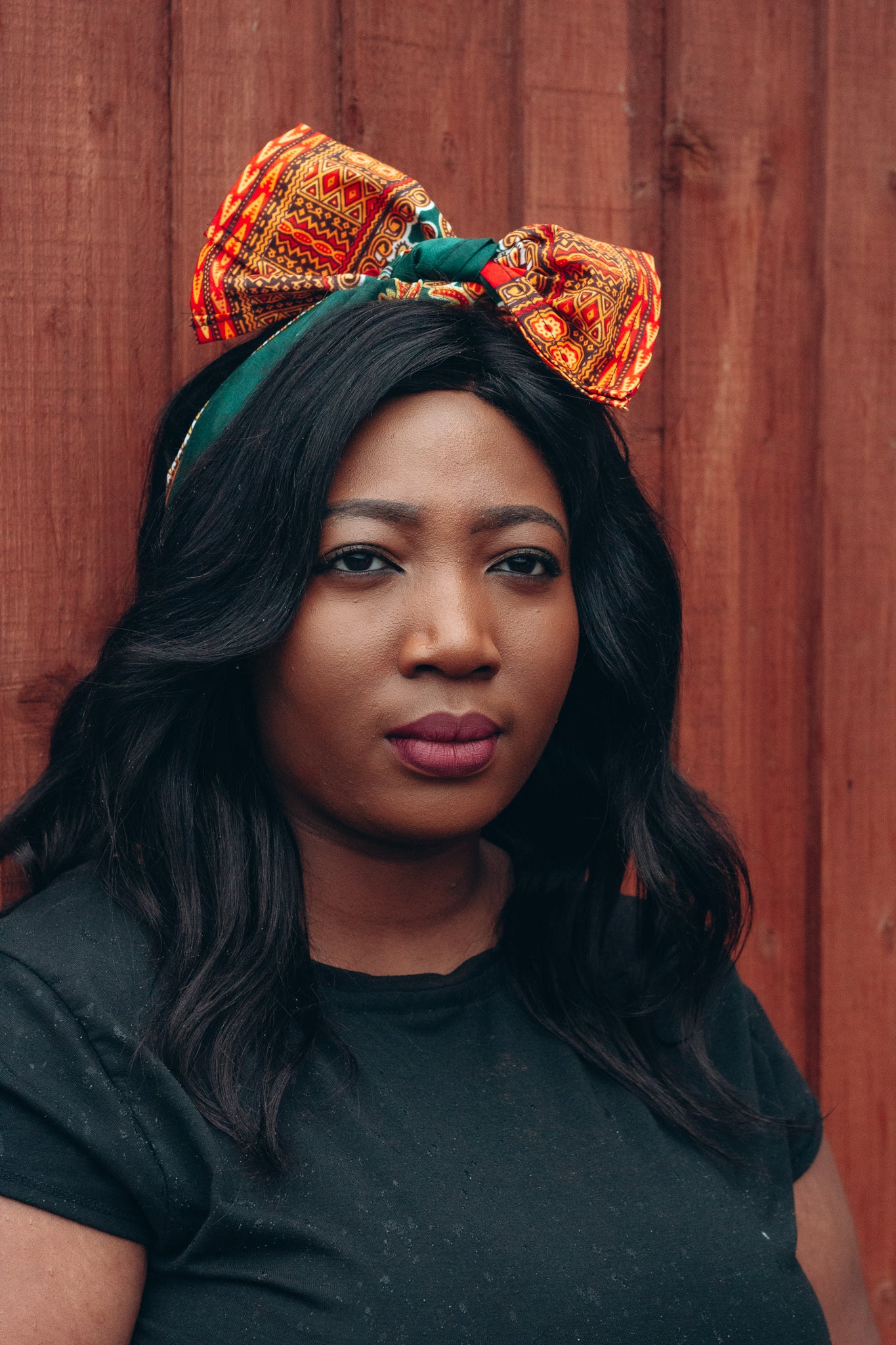 Orange, yellow, red and green African print head wrap tied as headband in a medallion panel pattern, made from sustainably sourced Ankara wax print. 