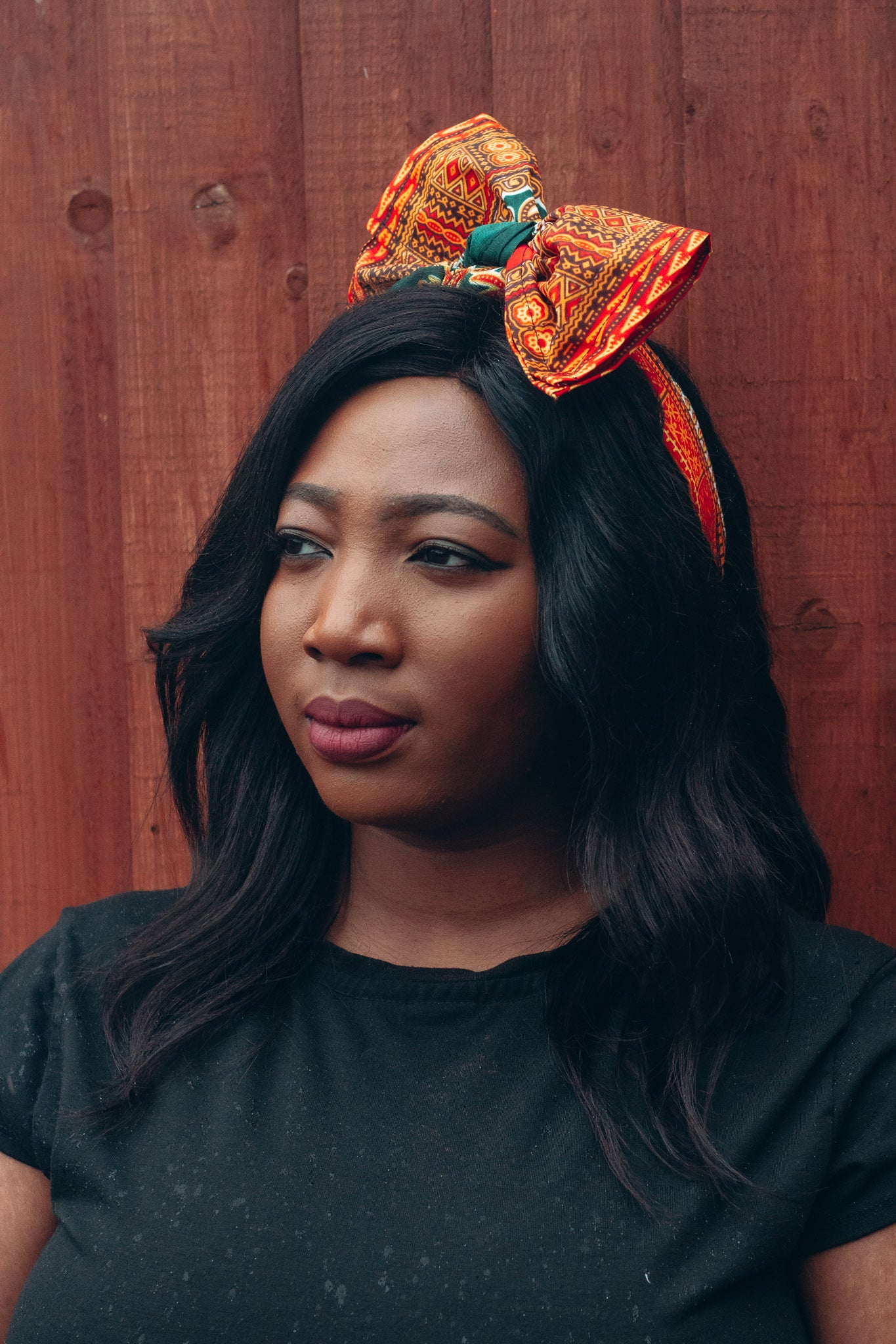 Orange, yellow, red and green African print head wrap tied as headband in a medallion panel pattern, made from sustainably sourced Ankara wax print. 