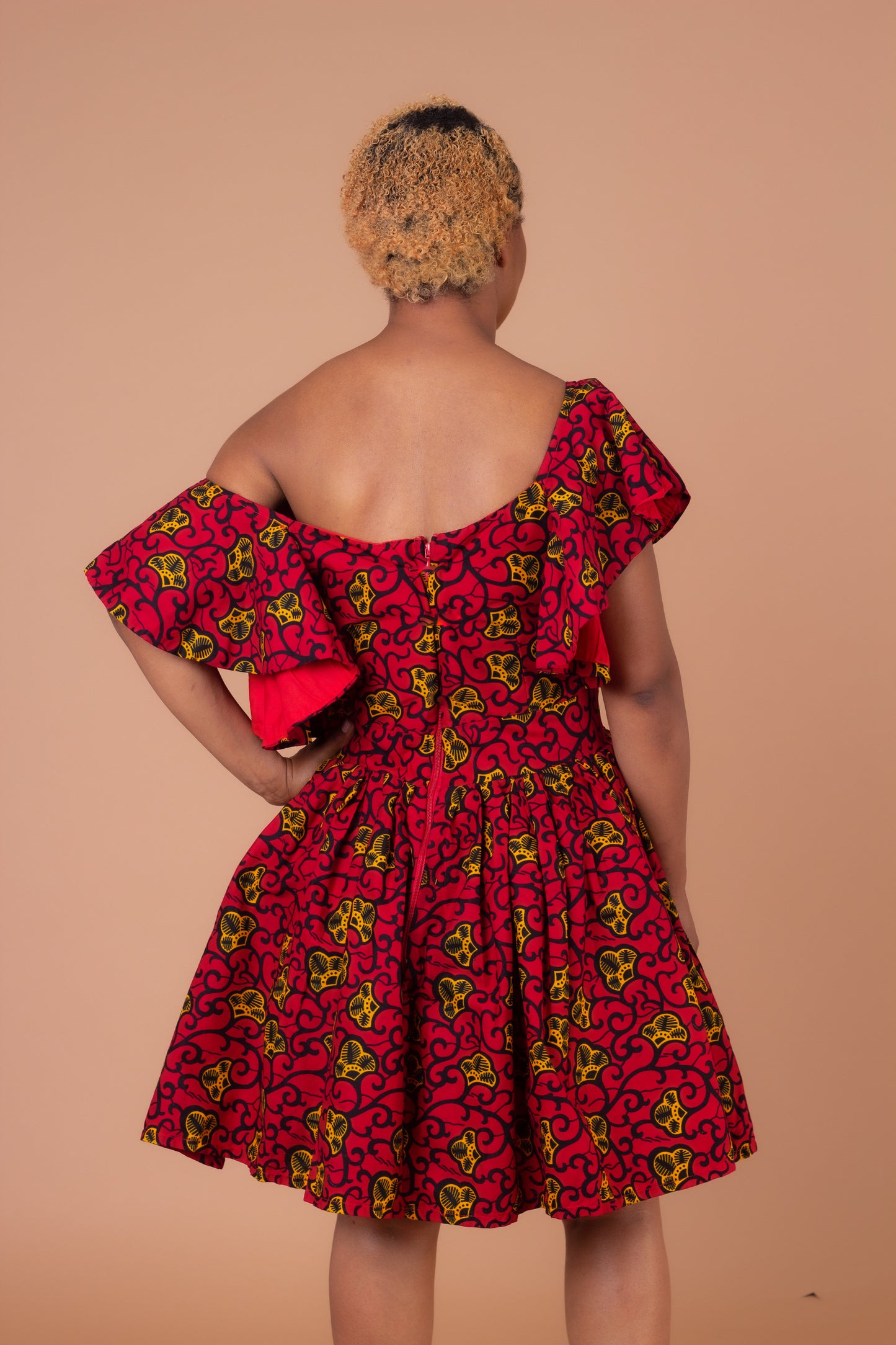   Red, yellow and black Ana African Ankara wax print in a floral pattern on a off the shoulder panelled ruffled skater dress with flared quarter sleeves with pockets on each side.