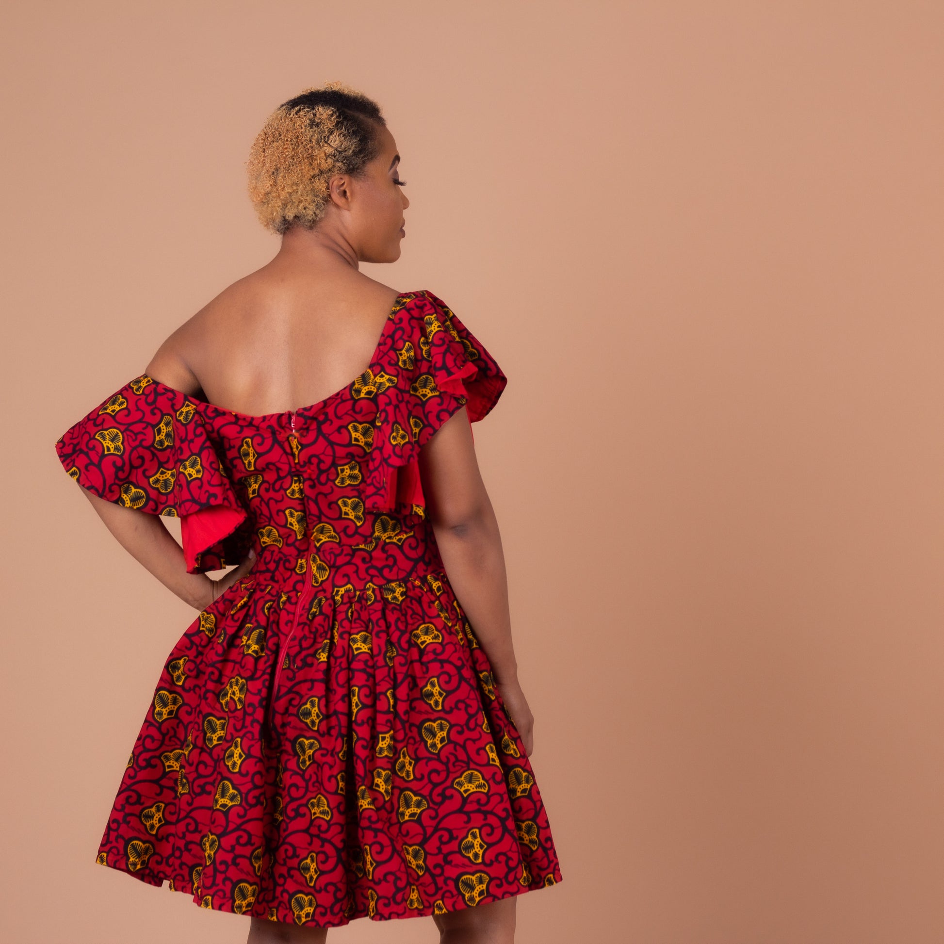   Red, yellow and black Ana African Ankara wax print in a floral pattern on a off the shoulder panelled ruffled skater dress with flared quarter sleeves with pockets on each side.