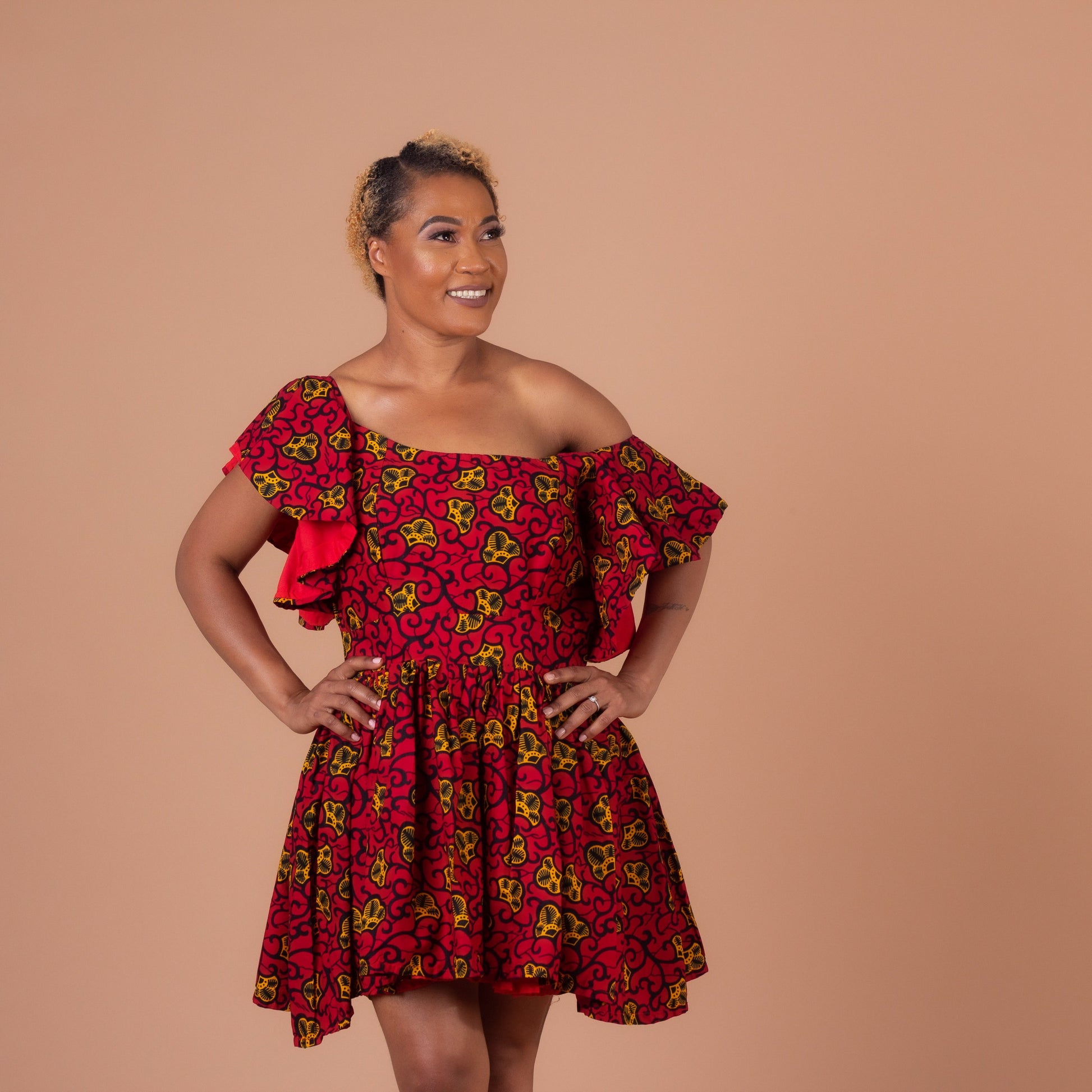   Red, yellow and black Ana African Ankara wax print in a floral pattern on a off the shoulder panelled ruffled skater dress with flared quarter sleeves with pockets on each side.
