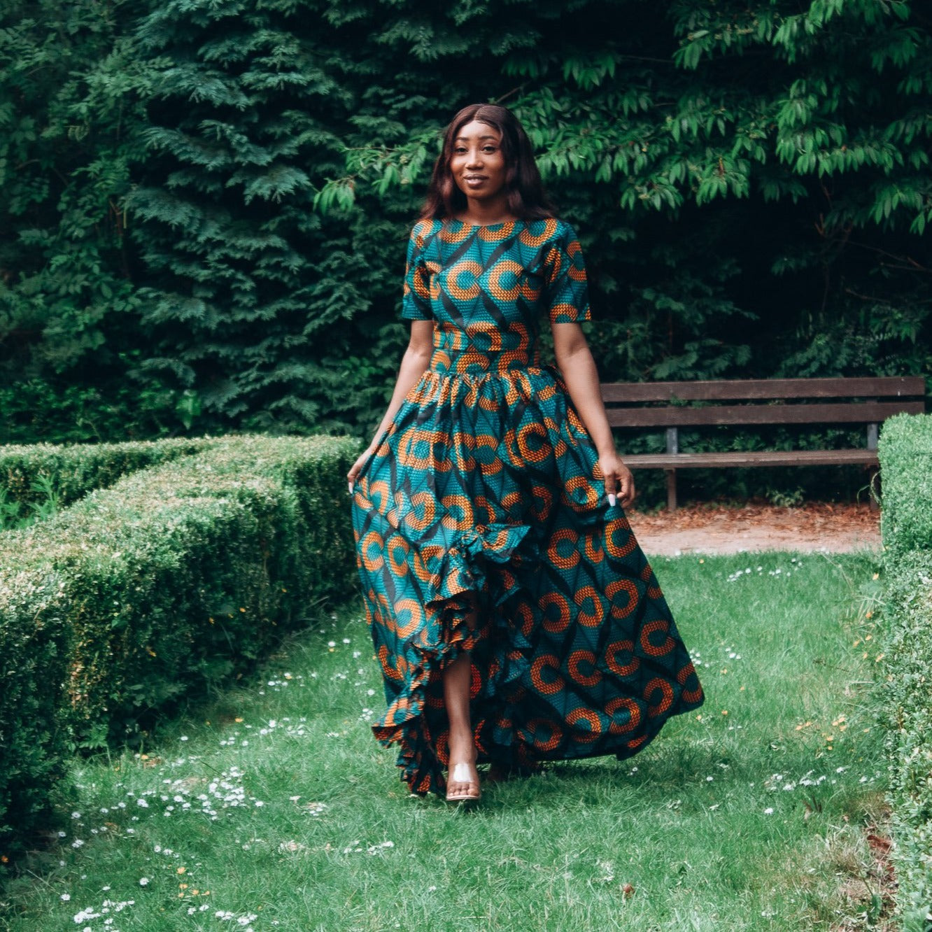 Orange, green and black African printed floor length high to low maxi skirt with a thigh high slit with ruffle detailed and seamed belt in a circle geo-shaped pattern, made from sustainably sourced Ankara wax print.