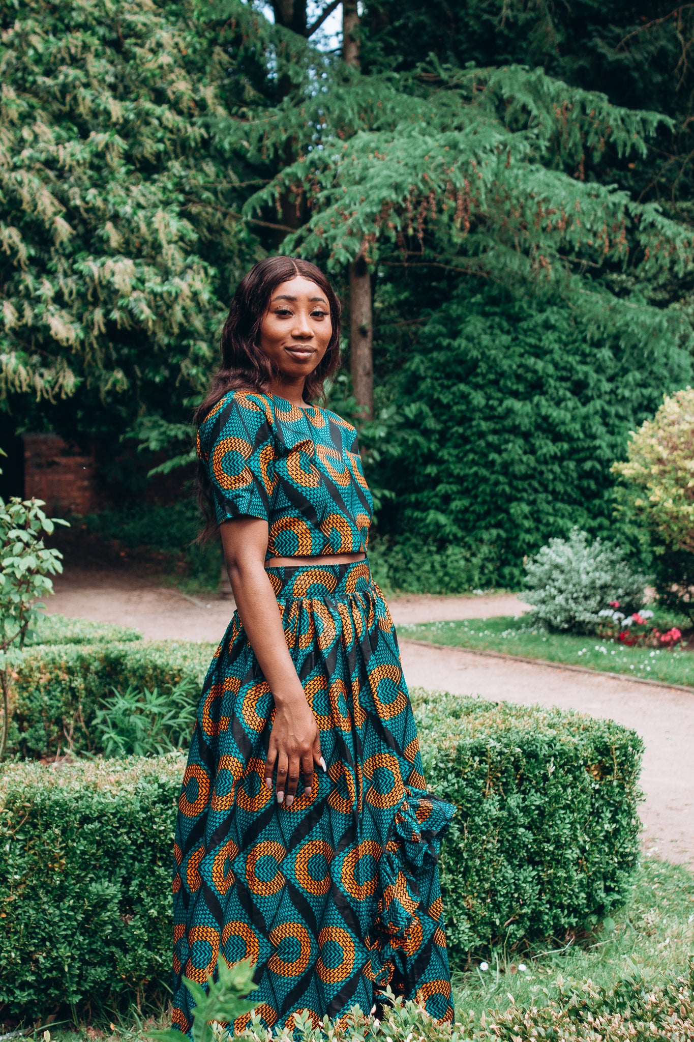 Orange, green and black African printed floor length high to low maxi skirt with a thigh high slit with ruffle detailed and seamed belt in a circle geo-shaped pattern, made from sustainably sourced Ankara wax print.