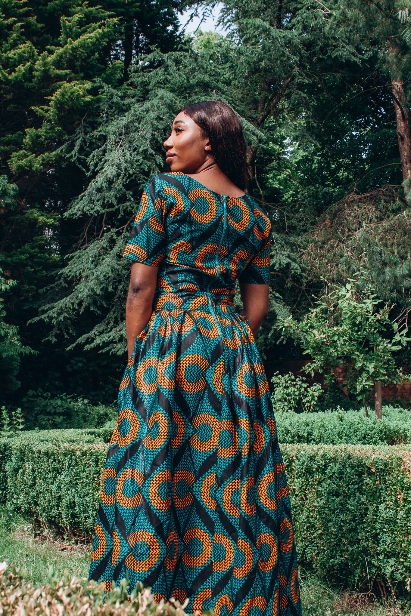 Orange, green and black African printed floor length high to low maxi skirt with a thigh high slit with ruffle detailed and seamed belt in a circle geo-shaped pattern, made from sustainably sourced Ankara wax print.