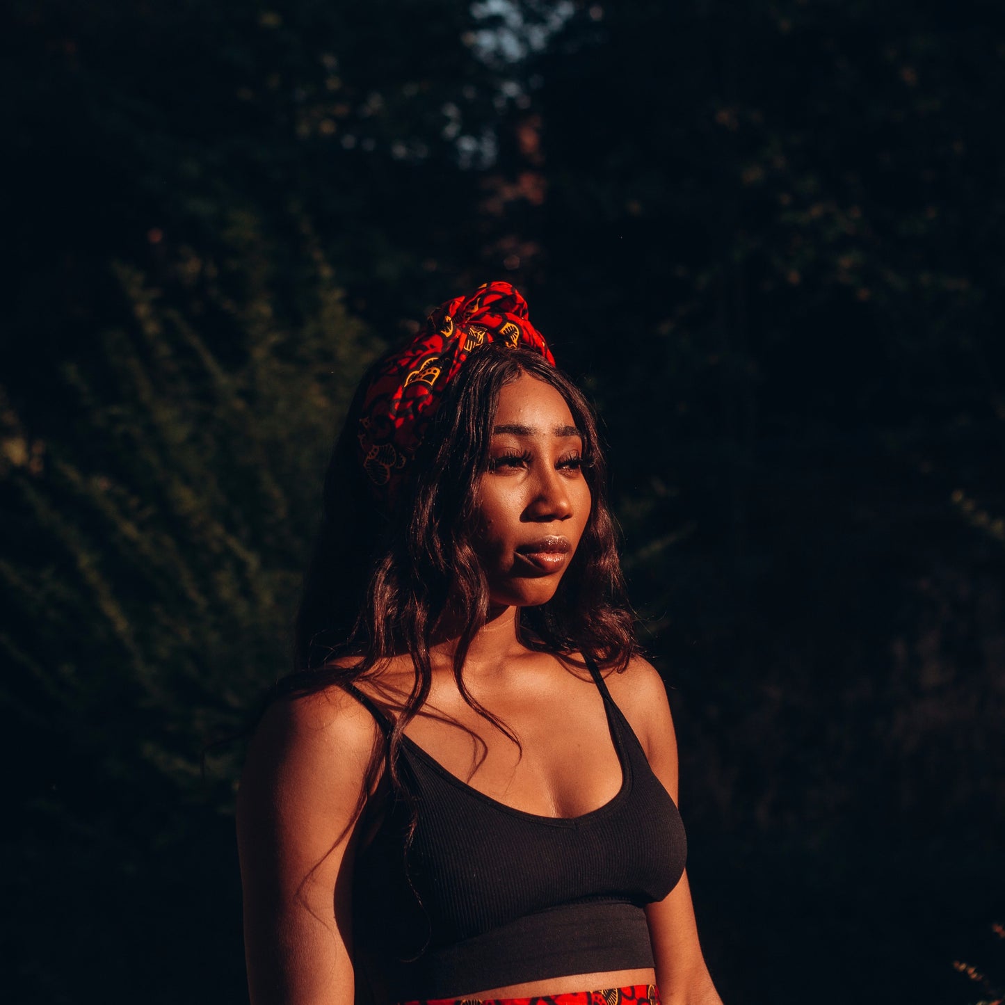 Red, yellow and black African print head wrap tied as headband in a floral pattern, made from sustainably sourced Ankara wax print. 