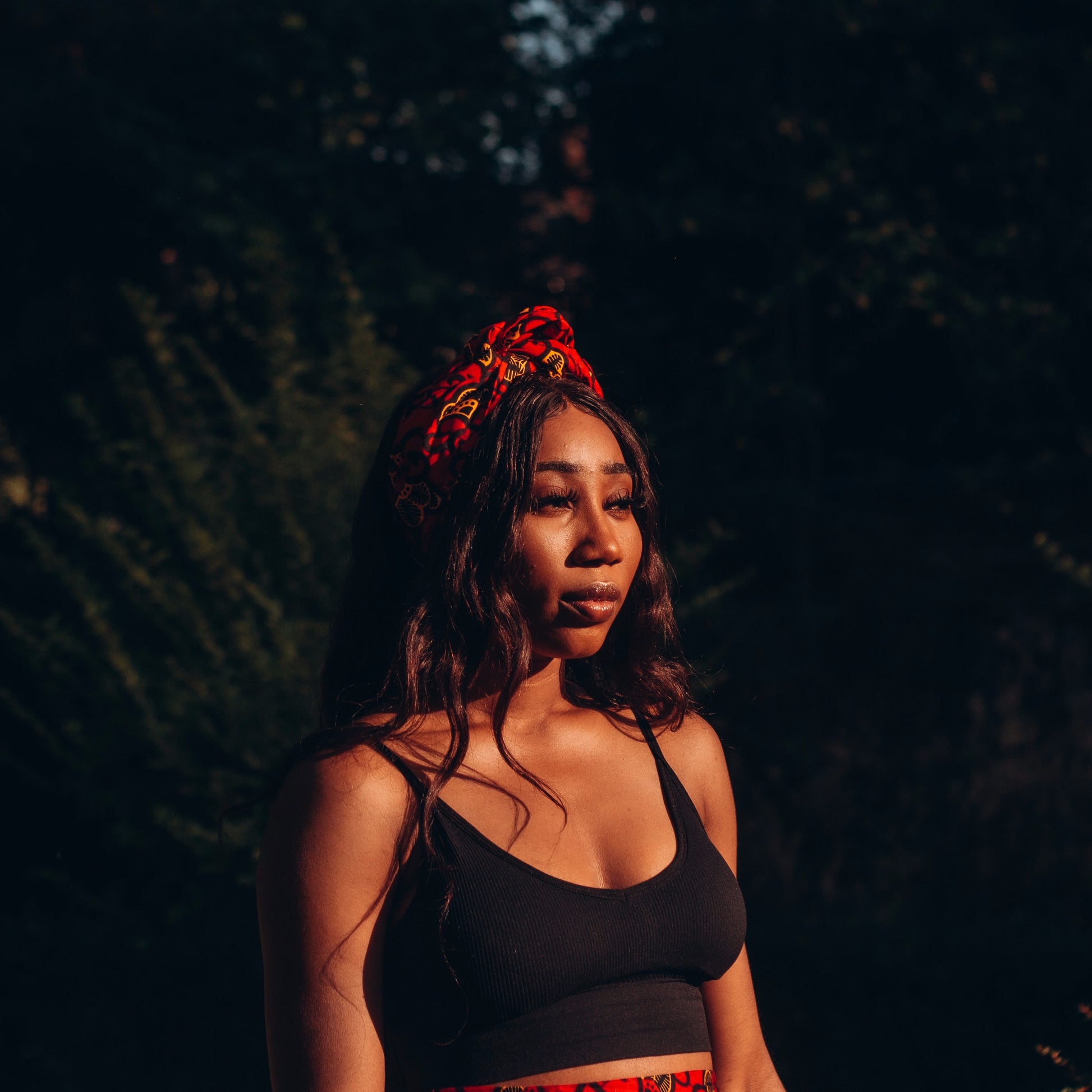 Red, yellow and black African print head wrap tied as headband in a floral pattern, made from sustainably sourced Ankara wax print. 