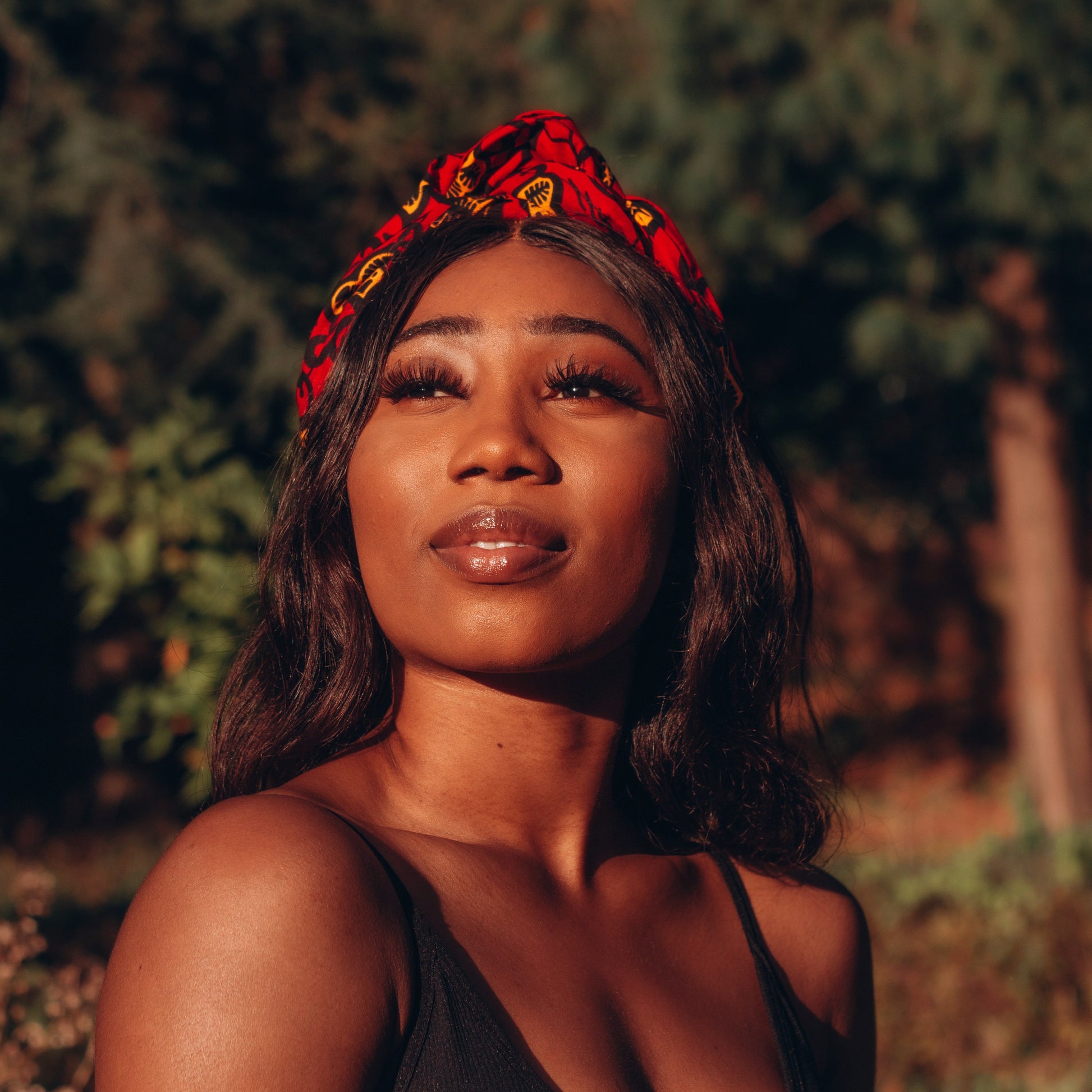 Red, yellow and black African print head wrap tied as headband in a floral pattern, made from sustainably sourced Ankara wax print. 