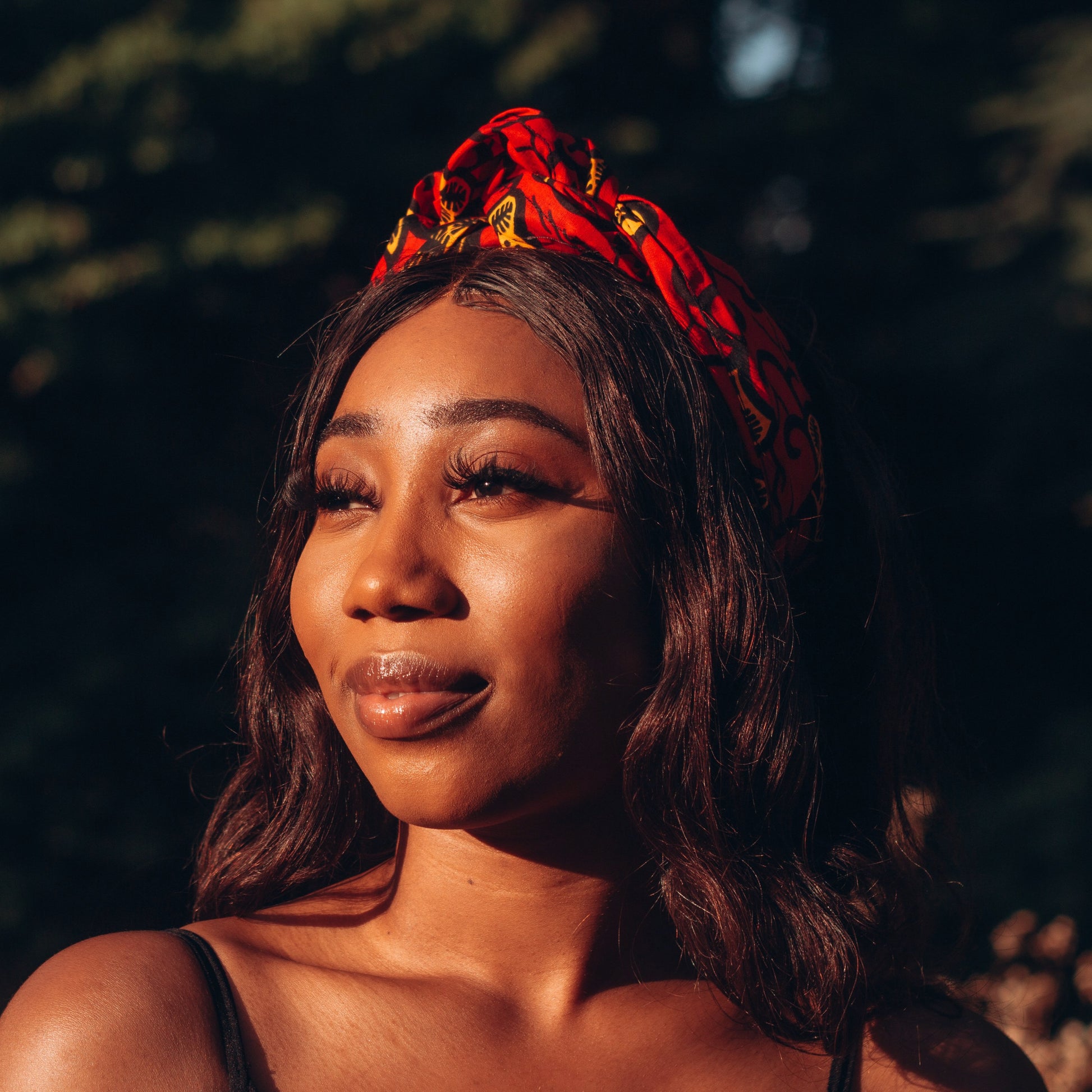 Red, yellow and black African print head wrap tied as headband in a floral pattern, made from sustainably sourced Ankara wax print. 