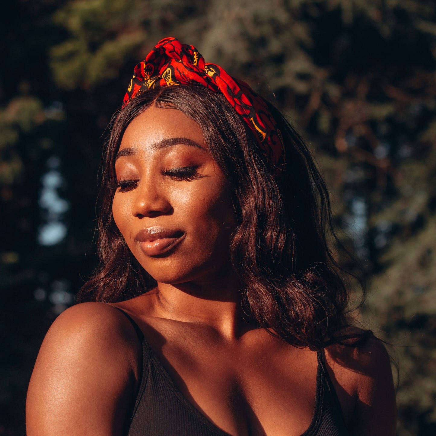 Red, yellow and black African print head wrap tied as headband in a floral pattern, made from sustainably sourced Ankara wax print. 