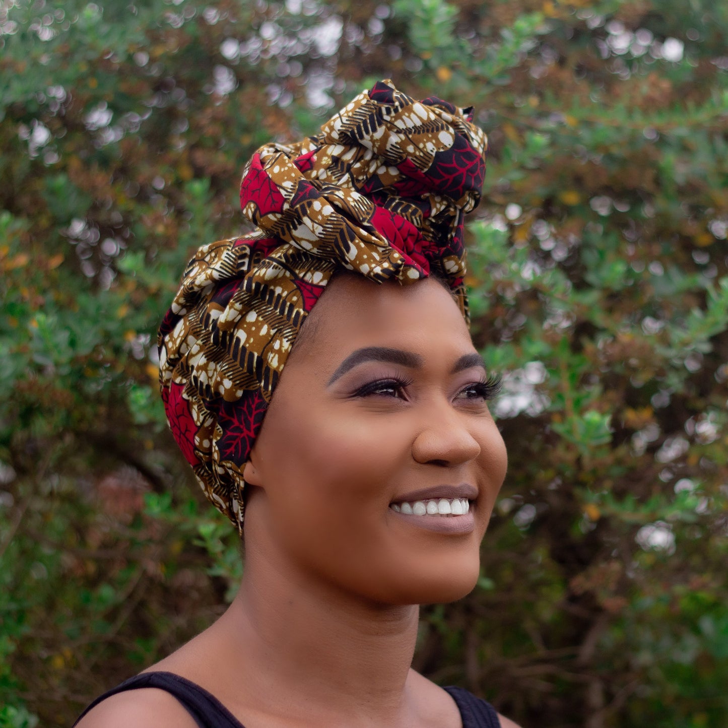 Brown, red, white, and black African print head wrap tied as a turban in a floral pattern, made from sustainably sourced Ankara wax print.