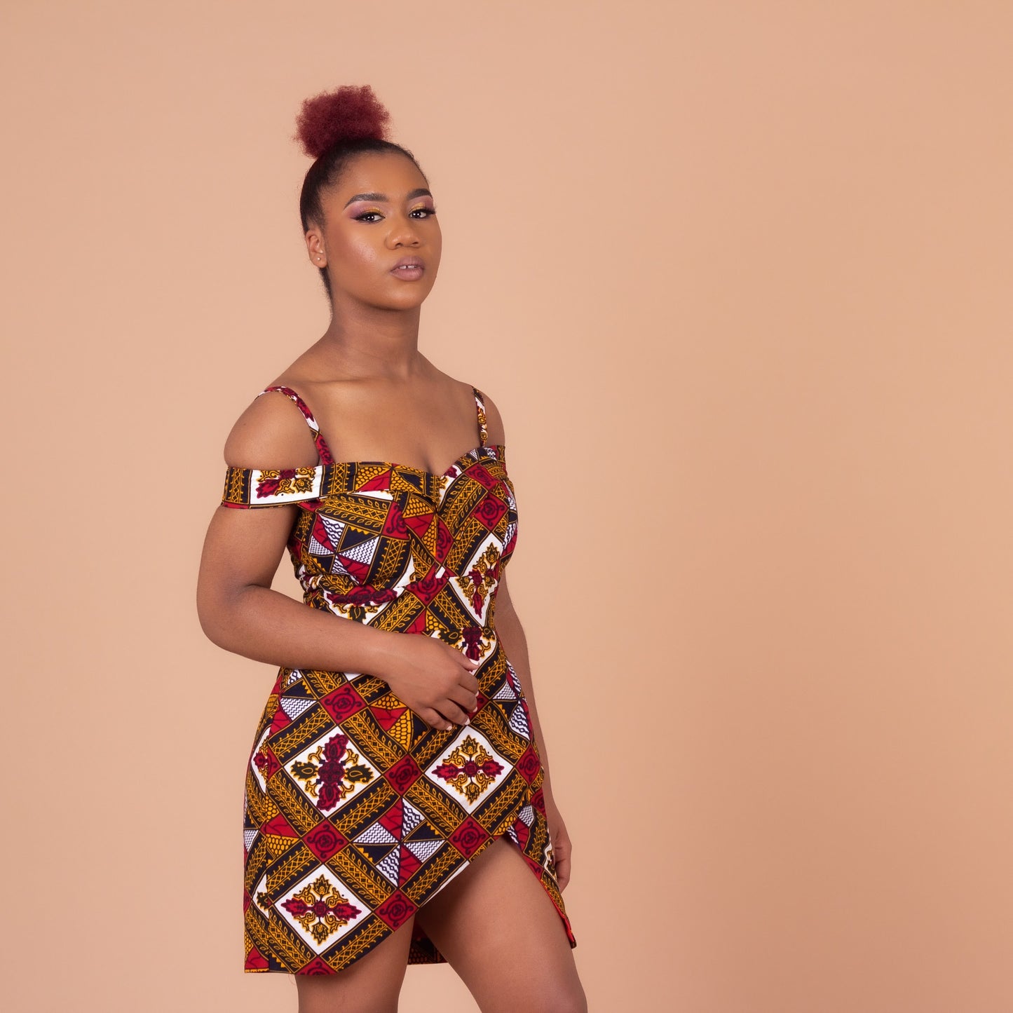 Red, yellow, white, and black Ankara wax print In African floral medallion pattern on a above knee high open pleated panelled dress with sweetheart neckline dress with off the shoulder straps, detailed with smaller spaghetti straps.