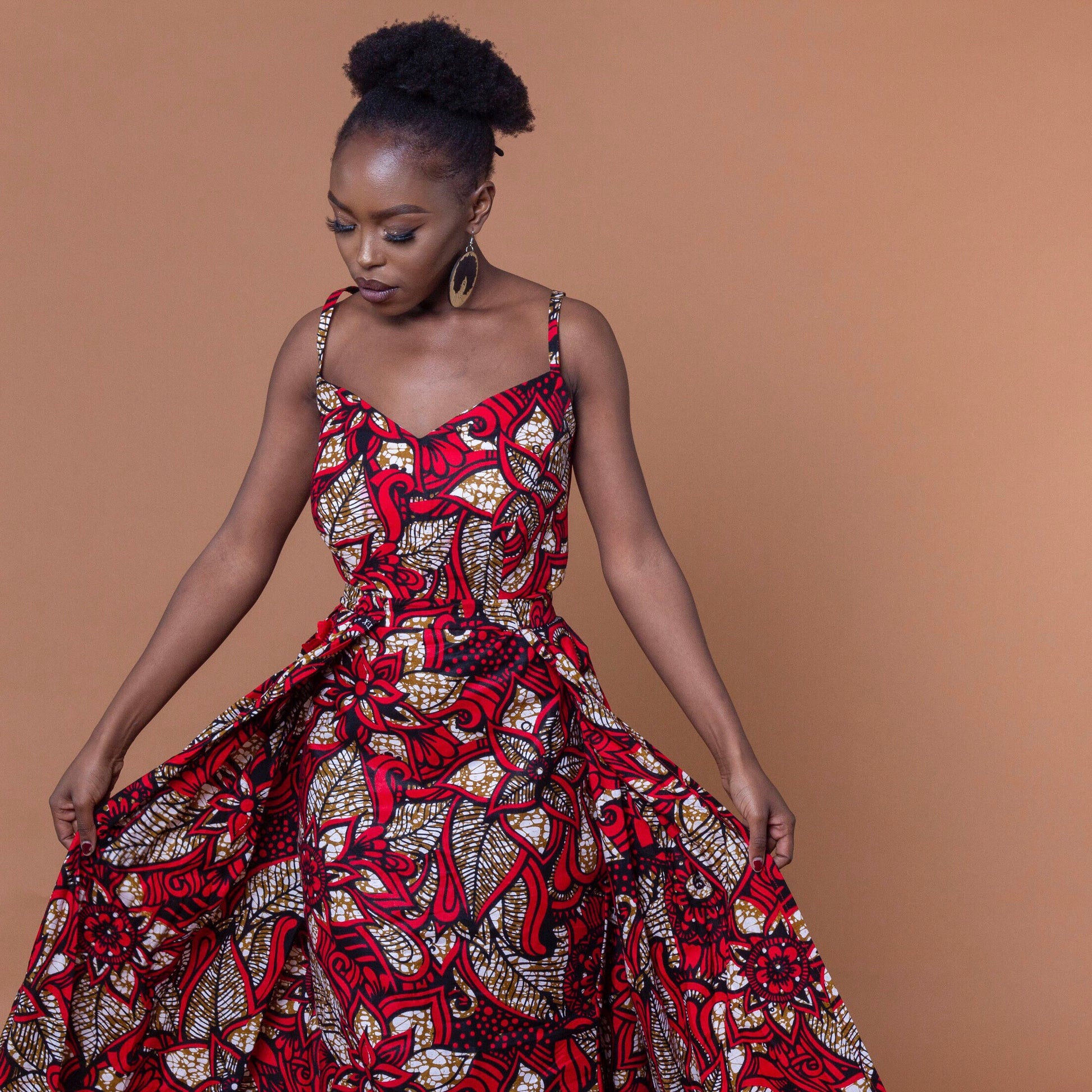 Ankara wax print in the bold African floral red, cream and light brown Ade fabric floor-length gown featuring a sweetheart neckline, closed back and off-shoulder straps with a matching outer cape belt.